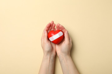 Female hands hold heart with adhesive plaster on beige background, top view