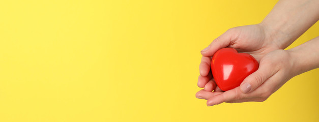 Female hands hold heart on yellow background. Health care, organ donation