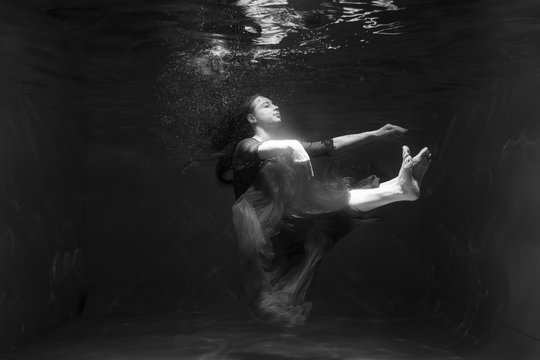 Black and white photo. Beautiful girl underwater in a red dress swims in the pool. Tenderness and elegance. Bubbles and a lot of water