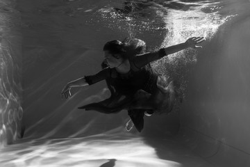 Black and white photo. Beautiful girl underwater in a red dress swims in the pool. Tenderness and elegance. Bubbles and a lot of water