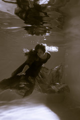 Black and white photo. Beautiful girl underwater in a red dress swims in the pool. Tenderness and elegance. Bubbles and a lot of water