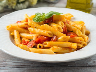Penne pasta with fresh tomatoes and basil on wooden table. Traditional italian dish