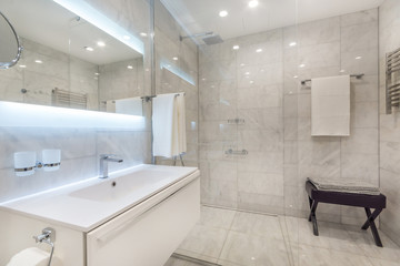 Beautiful modern bathroom with large backlit illuminated mirror, sink, and glass shower