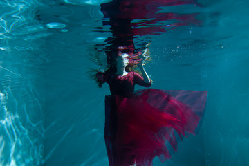 Beautiful girl underwater in a red dress swims in the pool. Tenderness and elegance. Bubbles and a lot of water