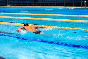 Athletic man swimming in butterfly style in the swimming pool with clear blue water.