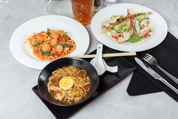 three-course set on a table in a restaurant, cafe menu. Business lunch from bowl ramen with chicken and egg, fresh caesar salad and pasta