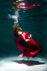 Beautiful girl underwater in a red dress swims in the pool. Tenderness and elegance. Bubbles and a lot of water