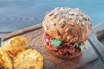 Delicious and juicy Burger as a symbol of American fast food and super-calorie diet. Served on a Board on a wooden background.