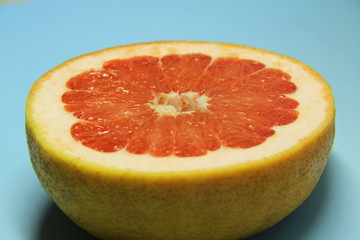 Half a juicy red grapefruit. Sliced aromatic delicious citrus fruit on a blue background.