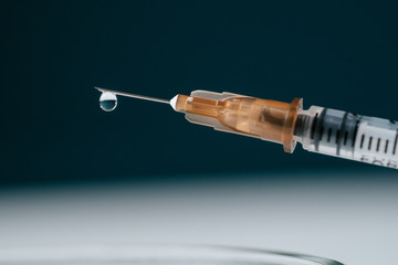 Close-up on a dark background of an insulin syringe, a drop of the drug is dripping from the needle. Diabetes treatment of the disease.