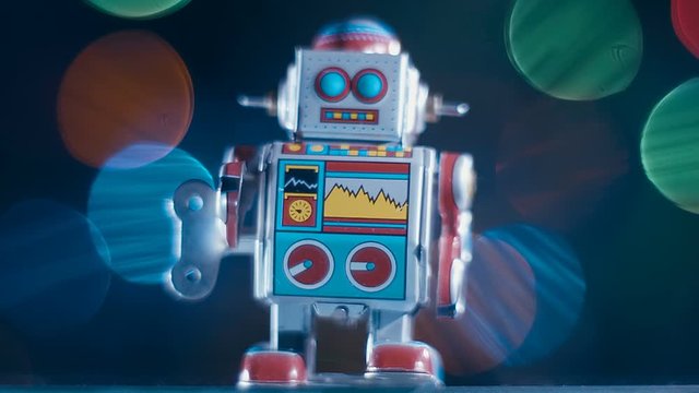 An antique cheerful colorful metal clockwork robot goes on a black background with colorful sparkling lights. Macro. Closeup. Shallow depth of field  