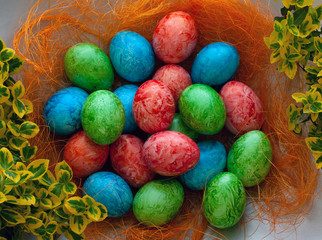 Colorful Easter holiday eggs, arranged with green twigs and an orange wreath of grass on a white background.