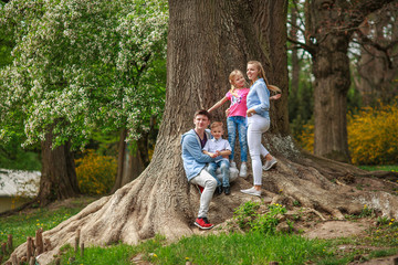Young family with two children daughter and son in botanical garden summer city park have a rest near tree in nature