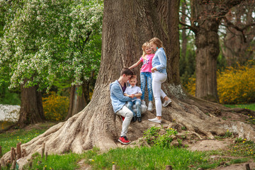 Young family with two children daughter and son in botanical garden summer city park have a rest near tree in nature