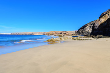 Fototapeta na wymiar View of beautiful Playa de la Cera beach, blue sea, yellow sand, cliffs. Papagayo, Playa Blanca, Lanzarote, Canary Islands, selective focus
