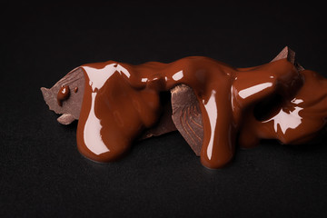 pieces of dark chocolate covered with melted cocoa on black table. sweet dessert