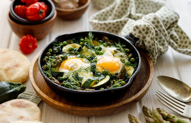 Green shakshuka with green vegetables and fried eggs in cast iron skillet on a white wooden table close up view