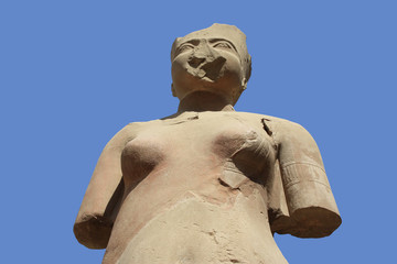 Fototapeta na wymiar The statue of a goddess in the ancient temple of Karnak in the Egyptian city of Luxor. Part of the sculpture is missing and the forearms have broken off. Blue sky and sunshine.