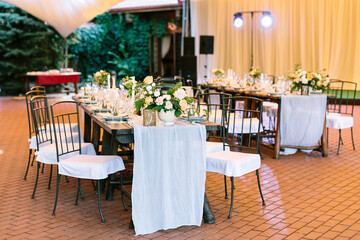 Side view, the line of the wedding table decorated with flower arrangements and sets of dishes. The style of the wedding is delicate and rustic.