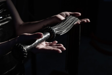 Close-up Black leather lash in female hands. Monochrome cropped photo of bdsms toys. A woman stands...