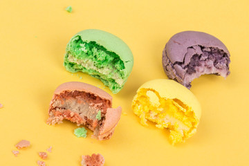 bitten colorful macaroons and crumbs on yellow background