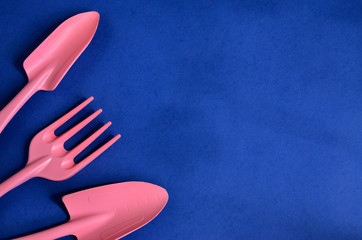 Garden equipment spatula and rake to care for plants on a blue background are lined on the left edge as a frame to copy space
