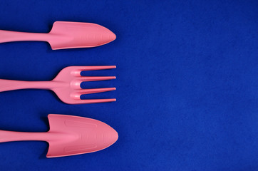 Garden equipment spatula and rake to care for plants on a blue background are lined on the left edge as a frame to copy space