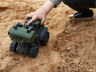 toy tractor and hand of a boy child. the kid plays in the sandbox with a toy. concept of child development, leisure or choice of future profession.
