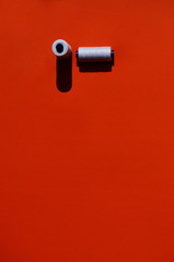 two coils with white sewing threads on an orange background with a shadow with a copy space