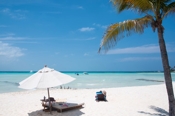 Blue sky Caribbean beach with palms and umbrella. White beach in Isla Mujeres, Mexico, America.