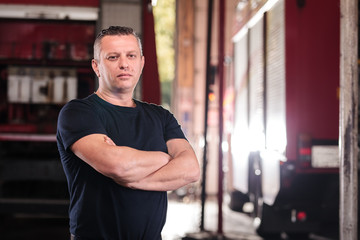 Fototapeta na wymiar Professional fireman portrait. Firefighter wearing shirt uniform and fire truck in the background.