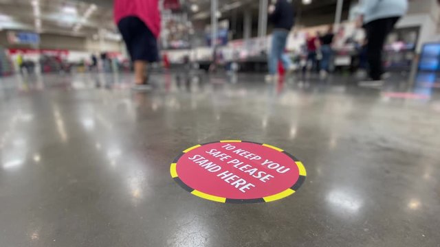 A low angle view of a social distance reminder sticker on the floor of a large big box warehouse store.	