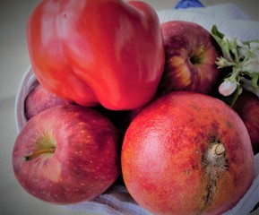 Still life of red fruits in a white kitchen towel (large ripe pomegranate, apples, peppers), on a light background and in natural daylight