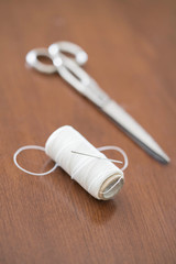 scissors and spool of white thread on wooden table