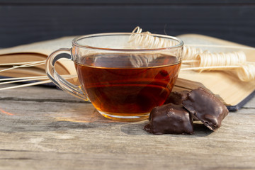 Cup of tea with open book and chocolate sweets on wooden background.