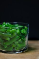 Fresh green string beans on a wooden Board with a black background in a glass Cup