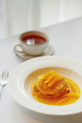 Pancake with orange on a white plate and tea
