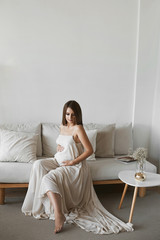 Pregnant model girl holding with love her belly and posing in a minimalist interior. Pregnant fashion concept