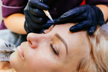 master brow artist makes permanent eyebrow makeup in the technique of powder browsers. Semi-permanent make-up