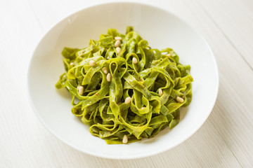 Close up Spinach Tagliatelle.  The Italian pasta with pine nuts and pesto sauce on wooden table.