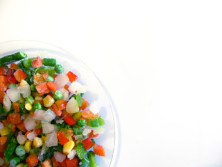 frozen vegetables (string beans, peas, corn, carrots, peppers) on a transparent plate on a white background. The view from the top.