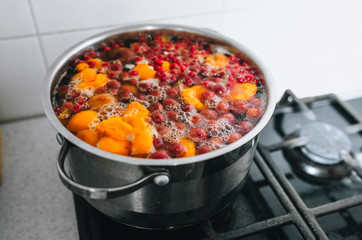 Cooking a delicious compote of apricot, apples, cherries, raspberries. Fresh fruits are boiled in boiling water in a metal pan on the stove. Photography, concept.