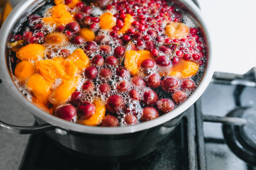 Cooking a delicious compote of apricot, apples, cherries, raspberries. Fresh fruits are boiled in boiling water in a metal pan on the stove. Photography, concept.