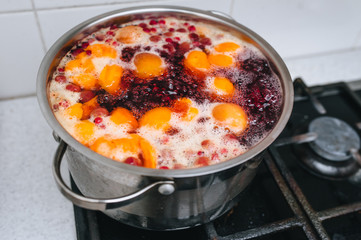 Fresh fruits are boiled in boiling water in a metal pan on the stove. Delicious stewed apricot, apples, cherries, raspberries. Photography, concept.