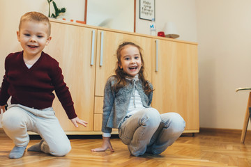 Lovely brother and his sister playing on the floor together in the living room while smiling and looking at camera