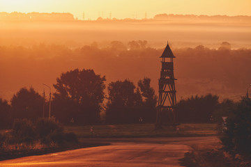 Foggy evening at sunset. Bluish fog in the sun. Ancient wooden tower in the middle of the road...