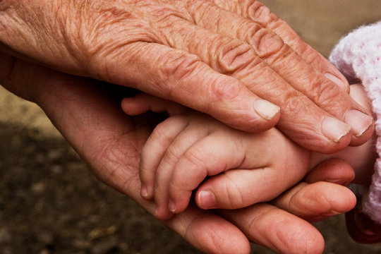Grandmother's old wrinkled hands gently touches the small arms of a child close-up. Little toddler is playing with an old grandmother. Hands of a child and old grandmother close-up