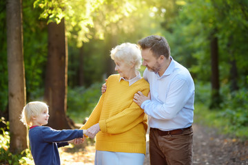 Beautiful eldery woman and her adult son, and her little grandson tenderly embracing together in...