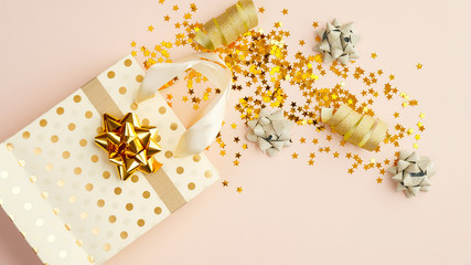 Flat lay golden confetti stars, party streamers, gift bag on beige table. Christmas, birthday or wedding celebration concept. Top view.