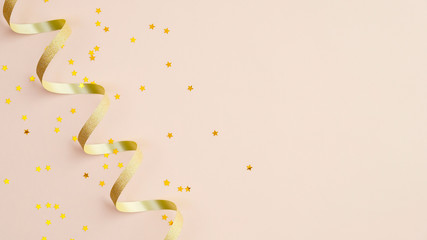 Golden spiral ribbon and confetti star on beige background. Christmas, birthday or wedding concept. Flat lay, top view.